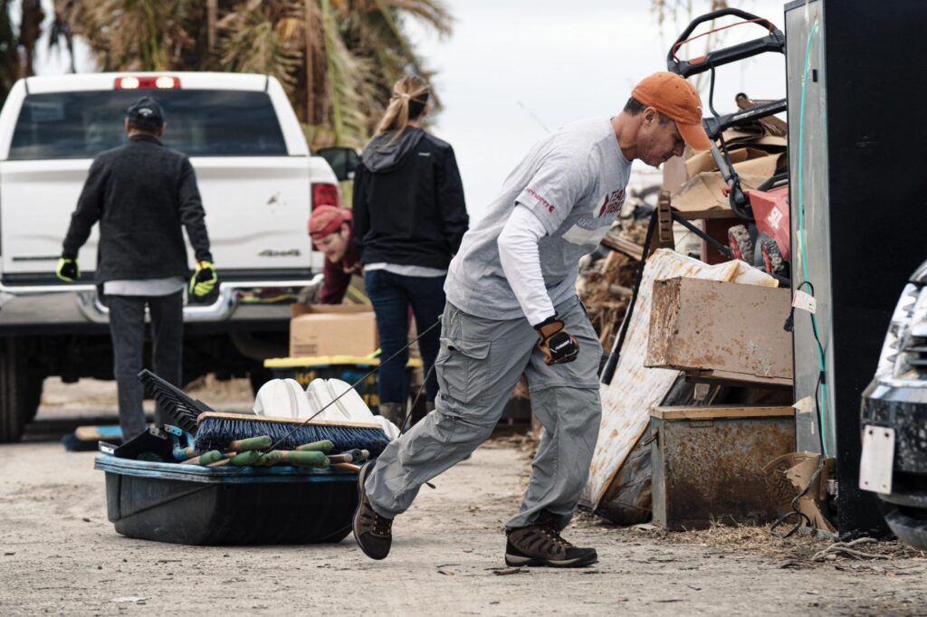 Man pulls sled with equipment past hurricane debris.
